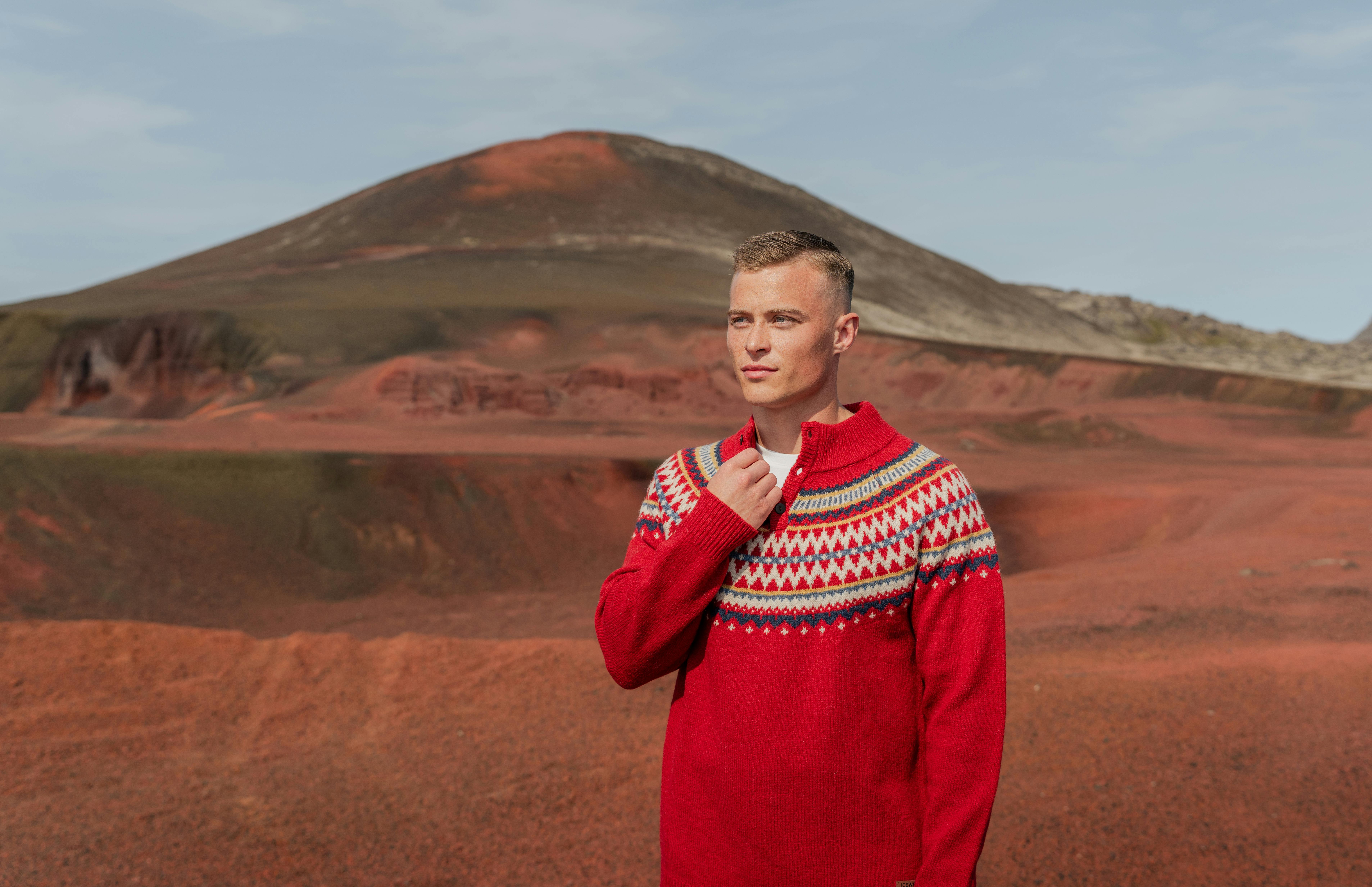 Man wearing wool sweater,small mountain behind him and red sand