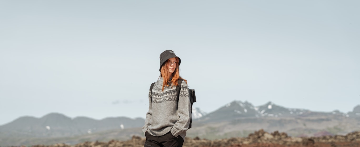 Une femme sur le sable rouge, l’ouest de l’Islande et les montagnes derrière elle