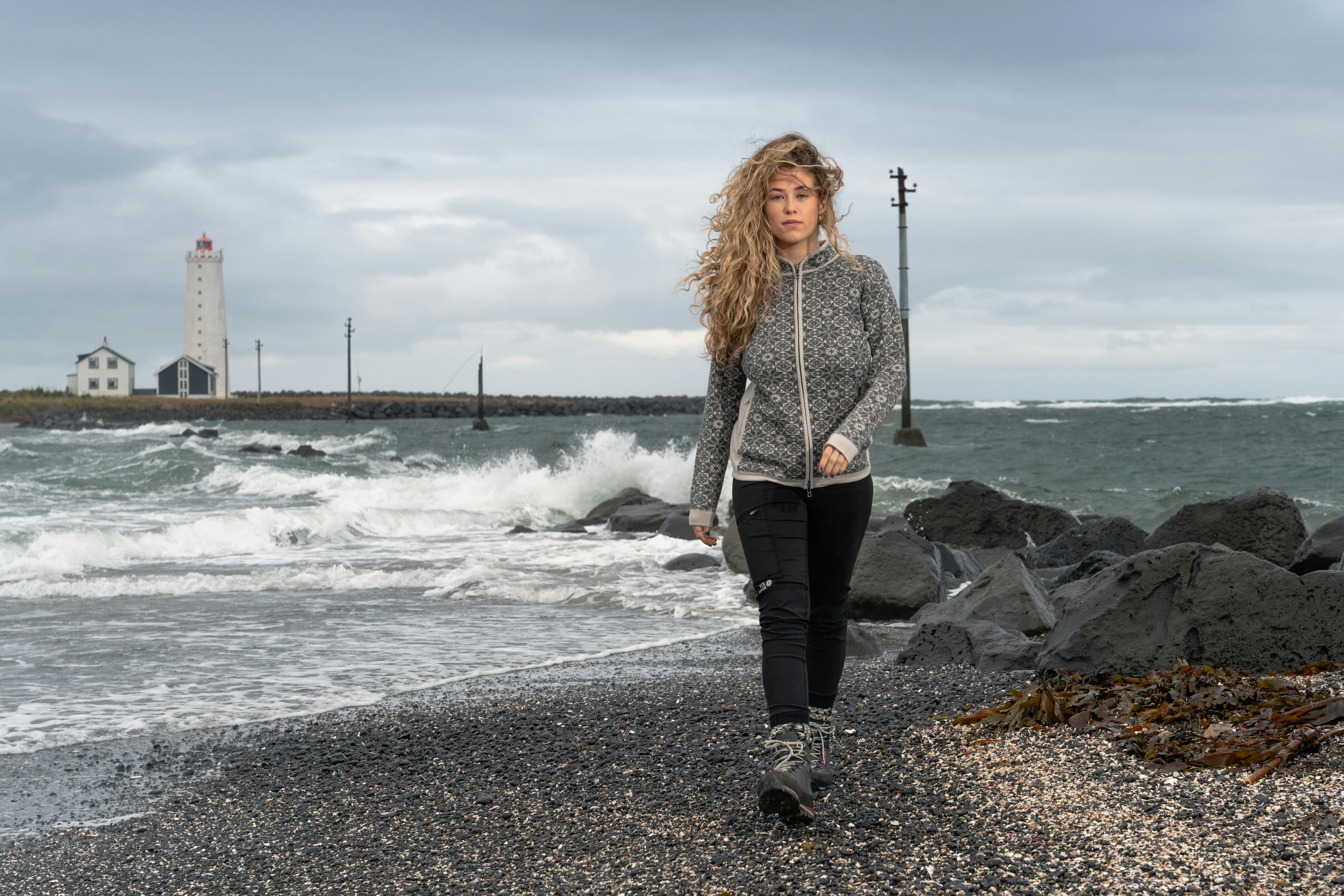 woman walking on rocky beach, old light house behind her