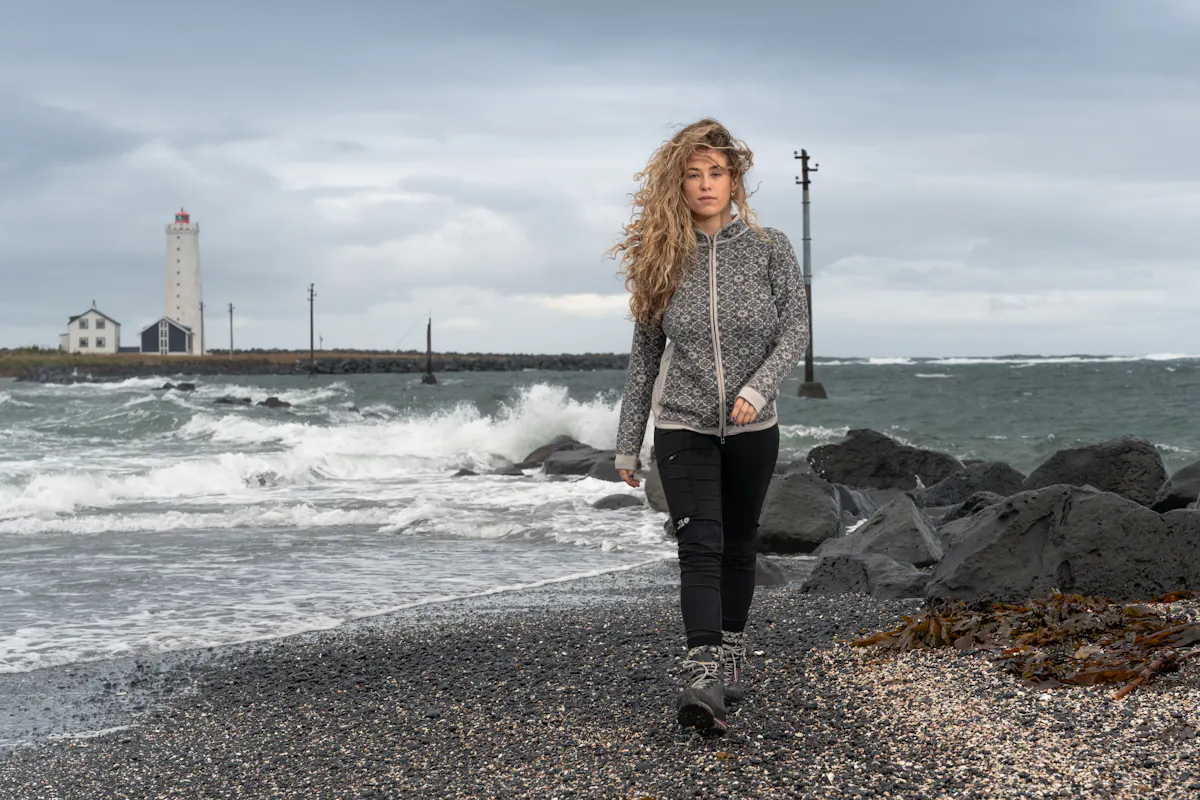 woman walking on rocky beach, old light house behind her