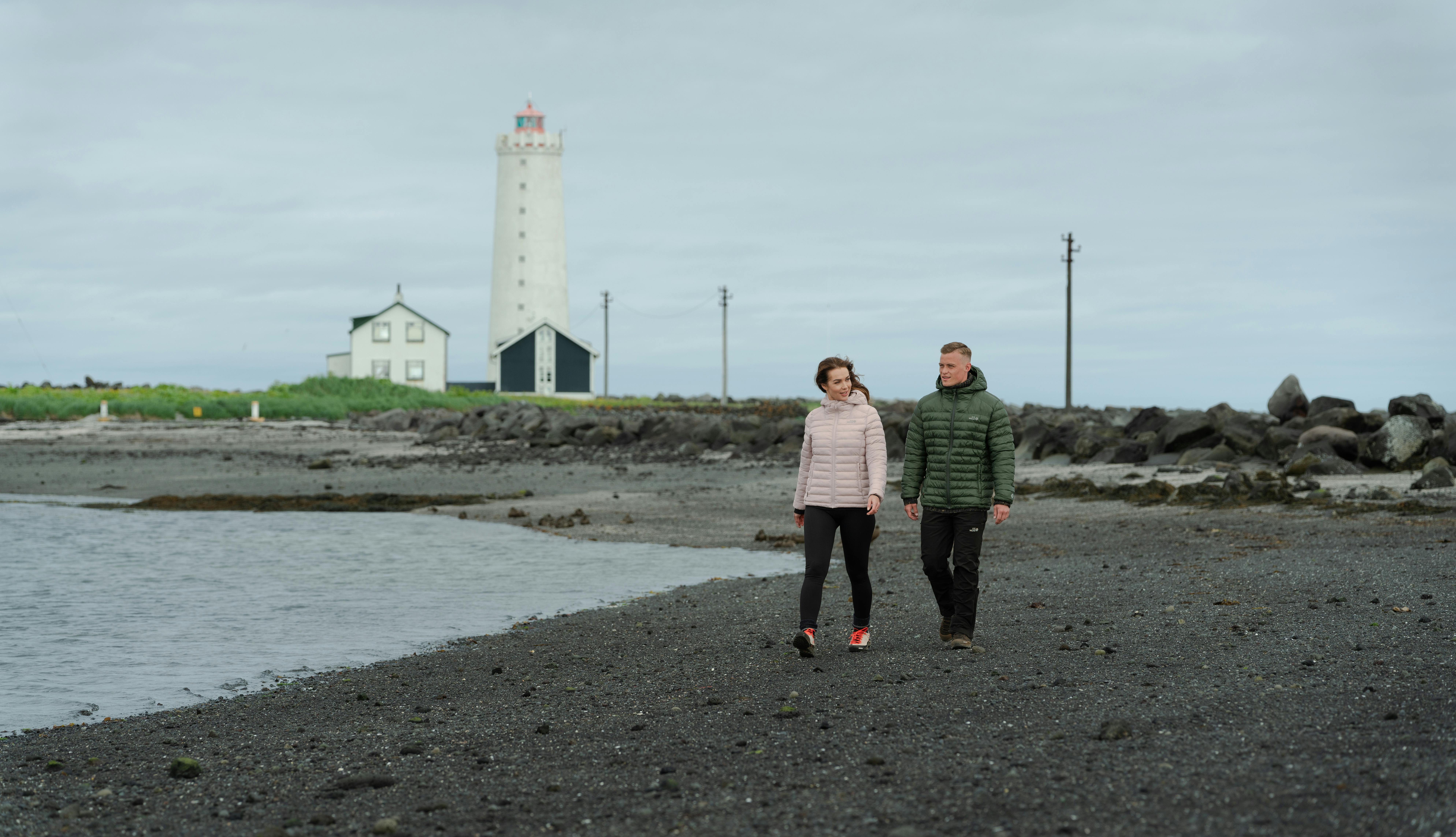 Un couple se promenant sur la plage, un vieux phare derrière eux