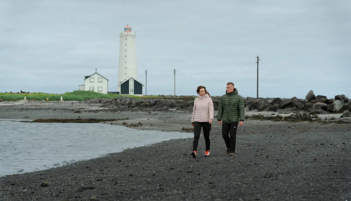 Un couple se promenant sur la plage, un vieux phare derrière eux