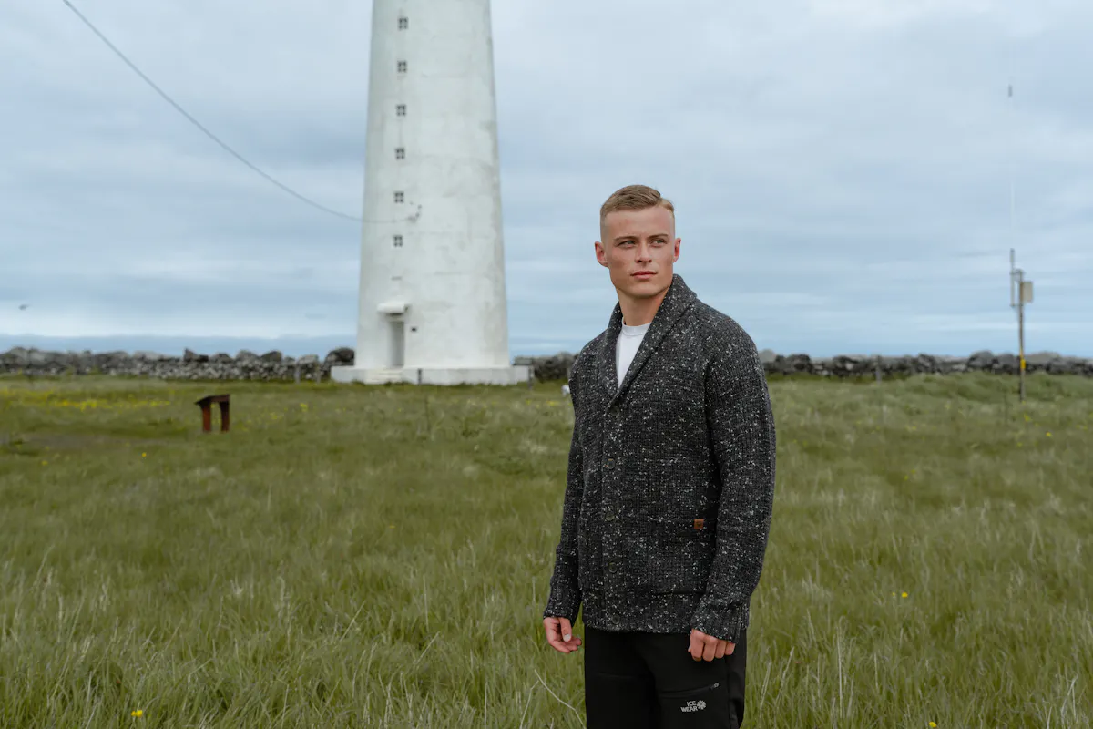 man in a gras field and light house behind him