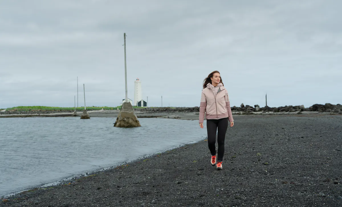 woman walking on the beach, old light house behind her