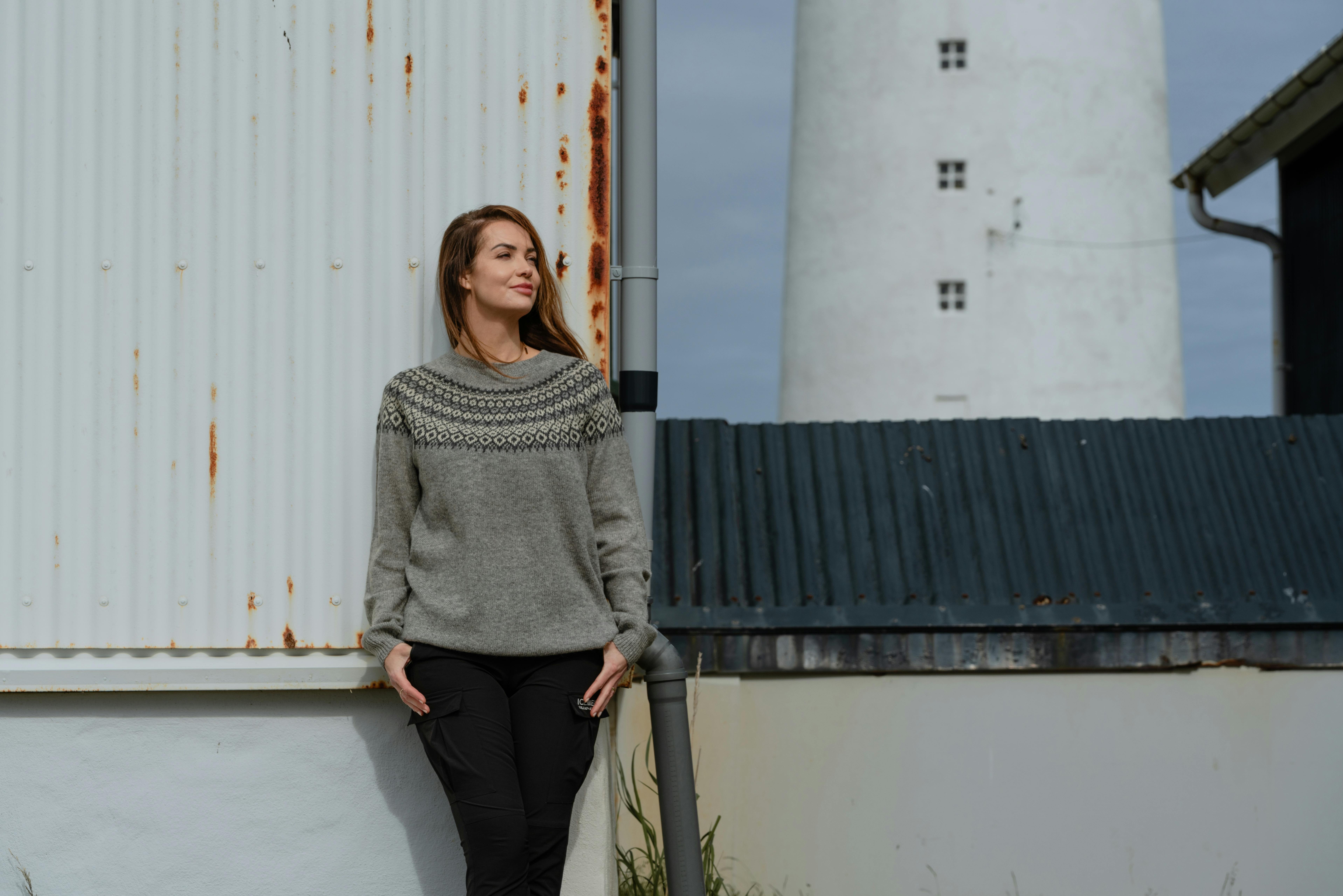 woman standing next to old rusty house with old light house behind her