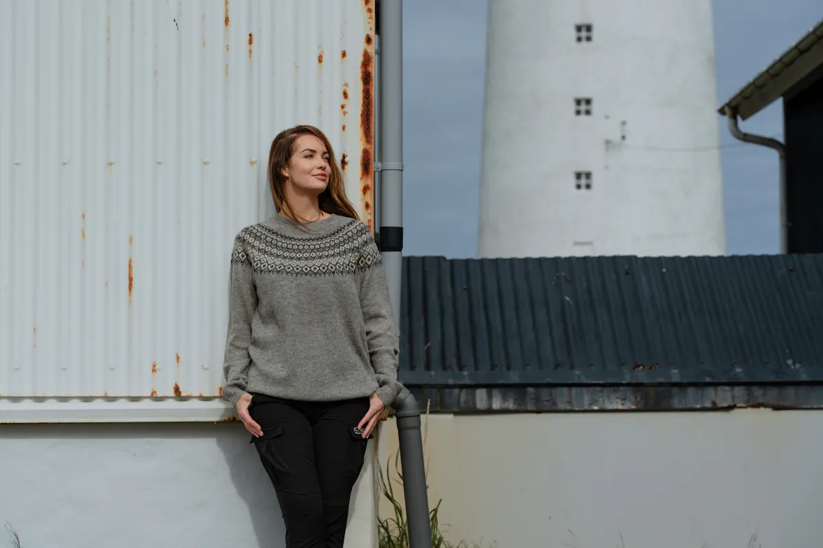 woman standing next to old rusty house with old light house behind her