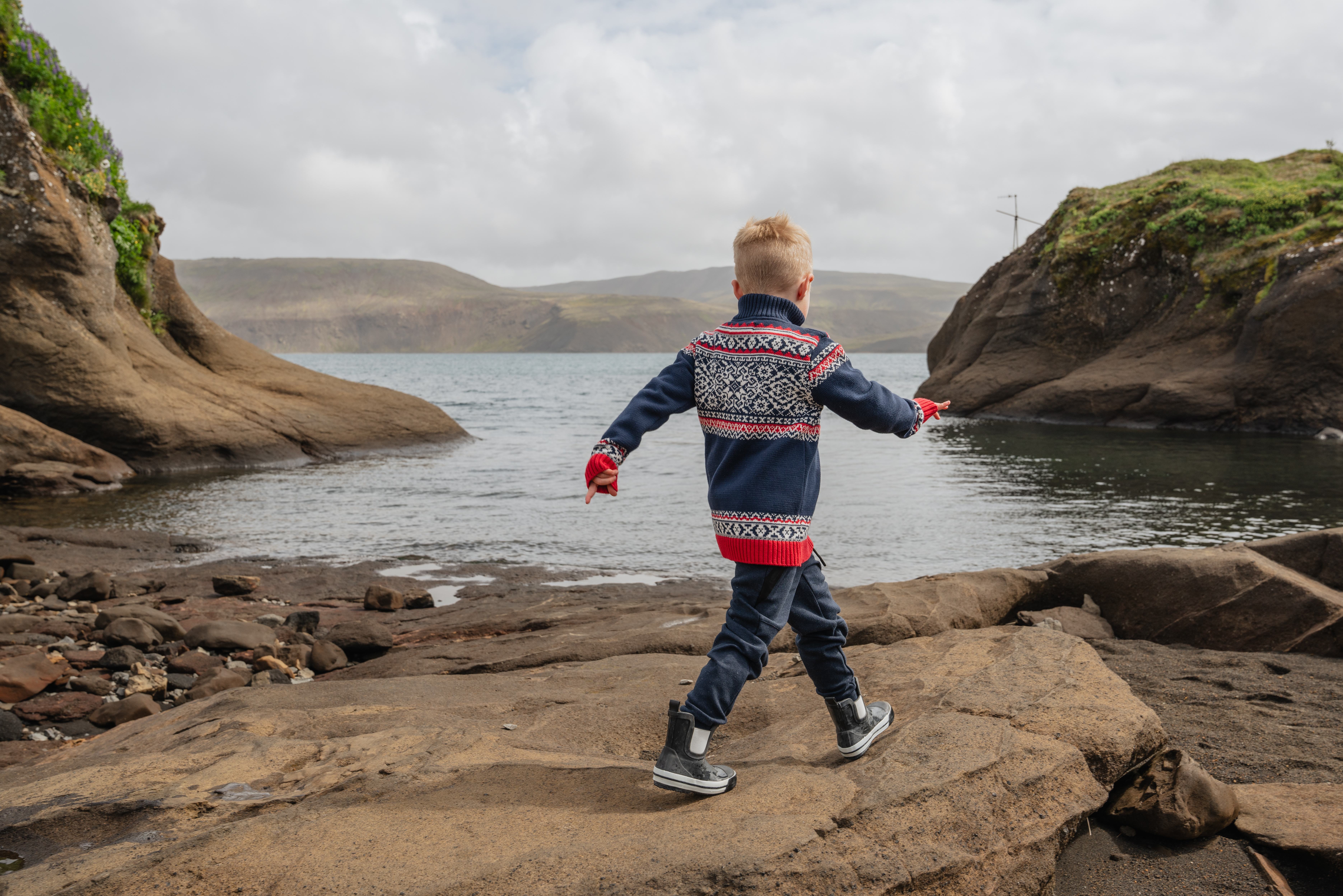 Boy walking on a cliff next to water