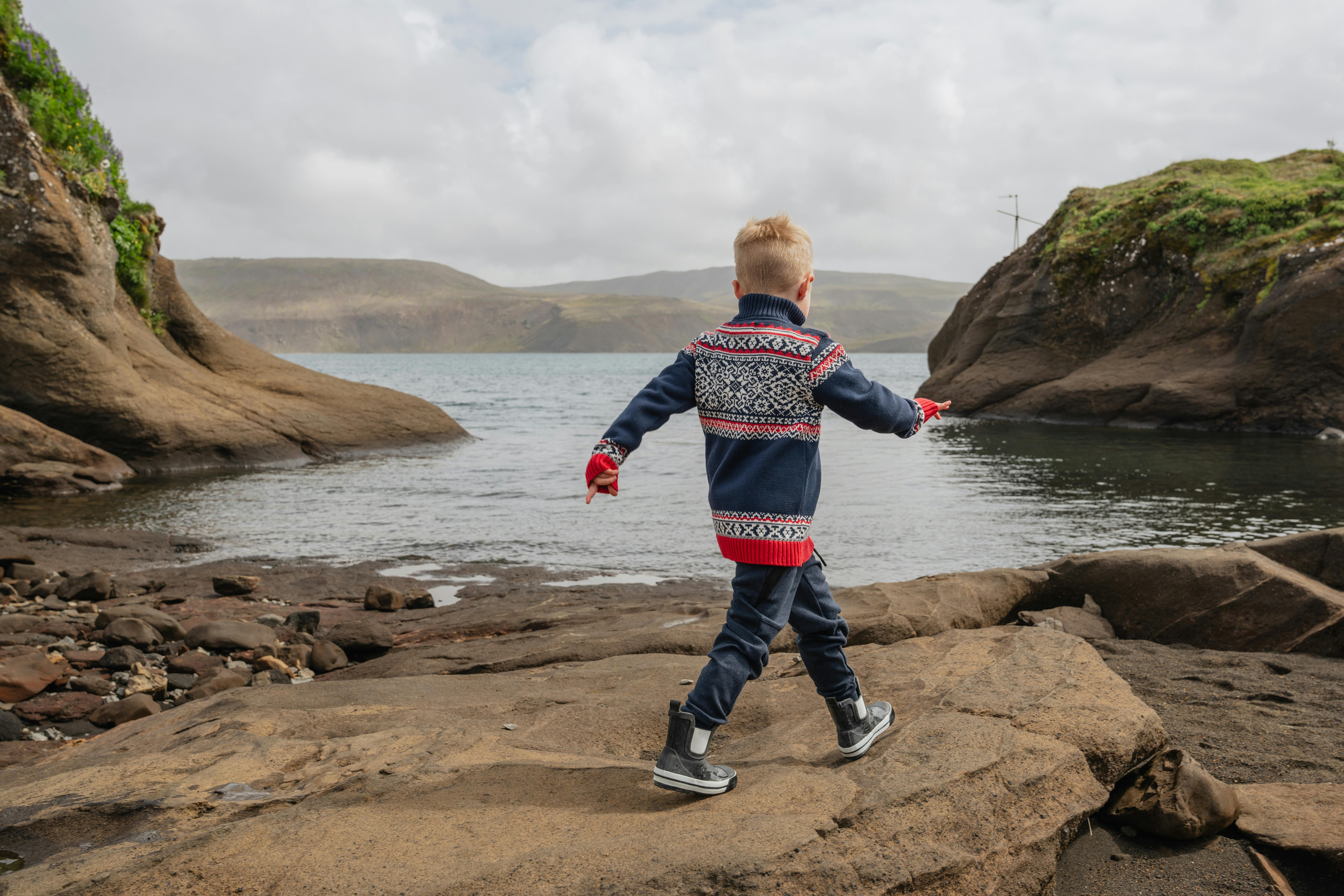 Boy walking on a cliff next to water