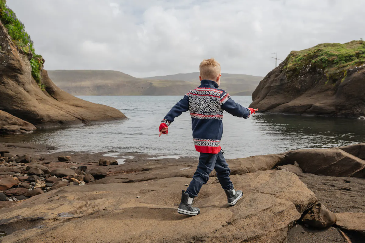 Boy walking on a cliff next to water