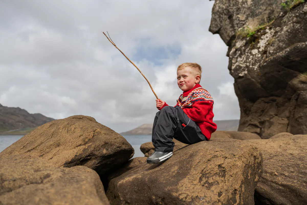 Garçon assis sur un rocher jouant avec des bâtons