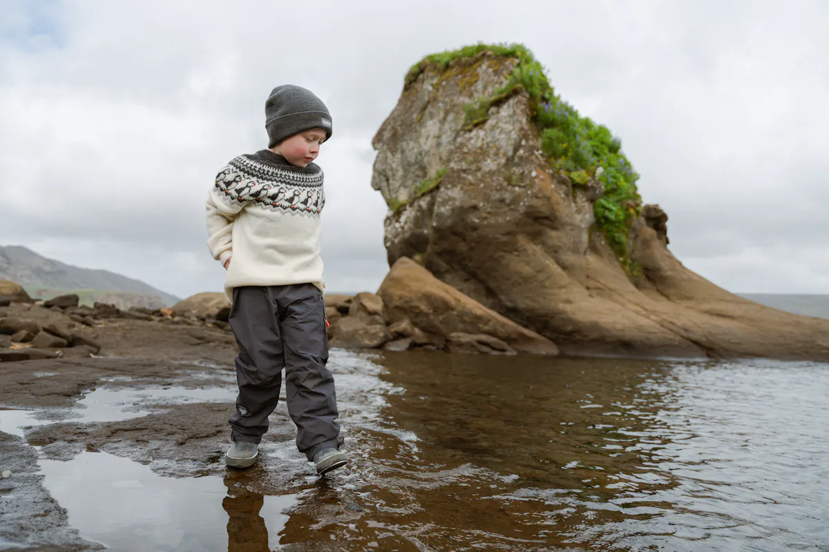 boy walking in a lake next to big cliff
