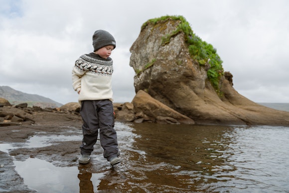 Junge geht in einem See neben einer großen Klippe spazieren