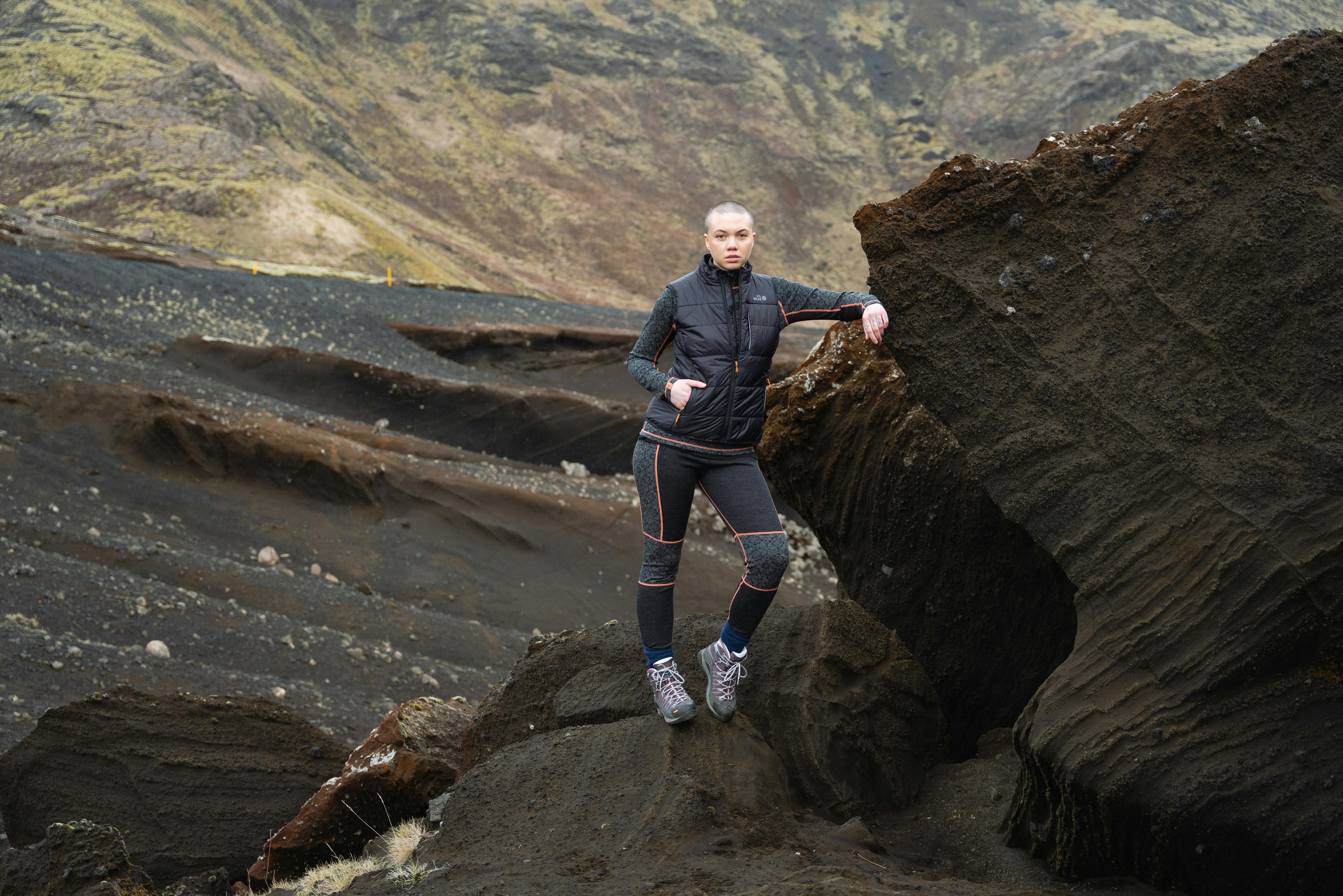 woman standing next to a cliff, wearing wool first layer and vest