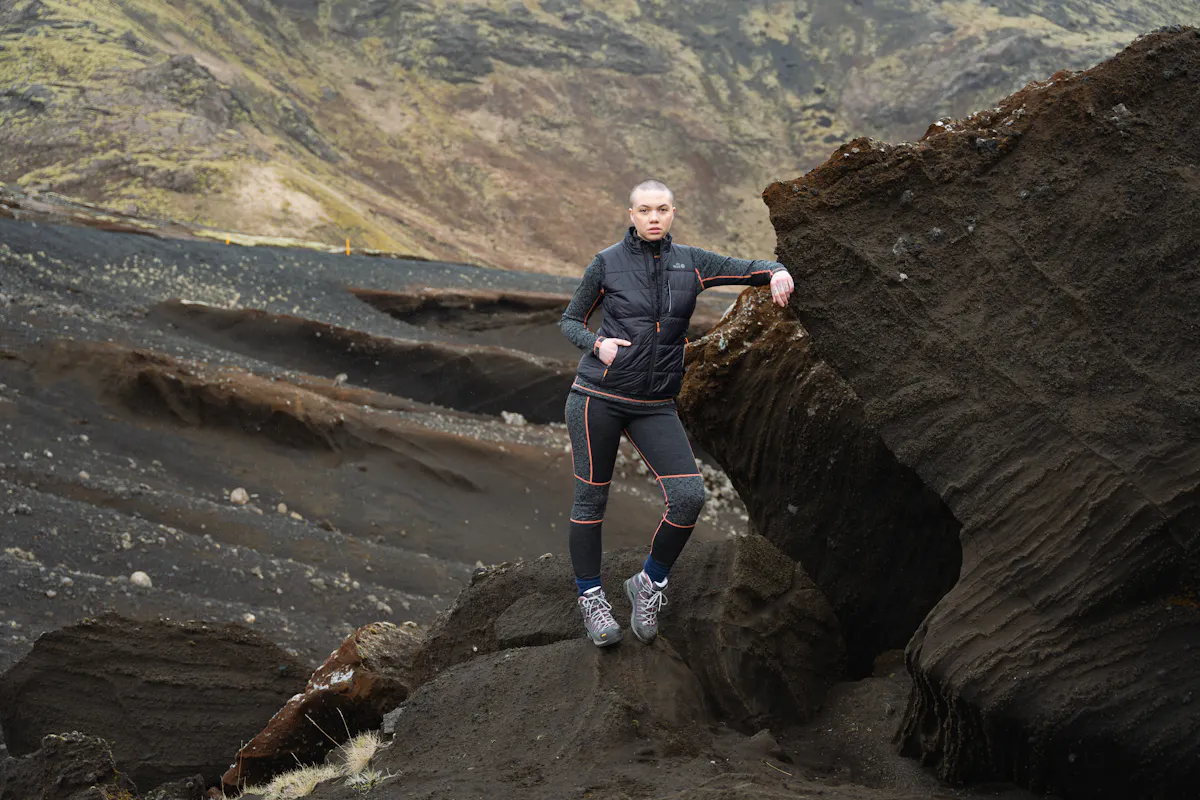 woman standing next to a cliff, wearing wool first layer and vest