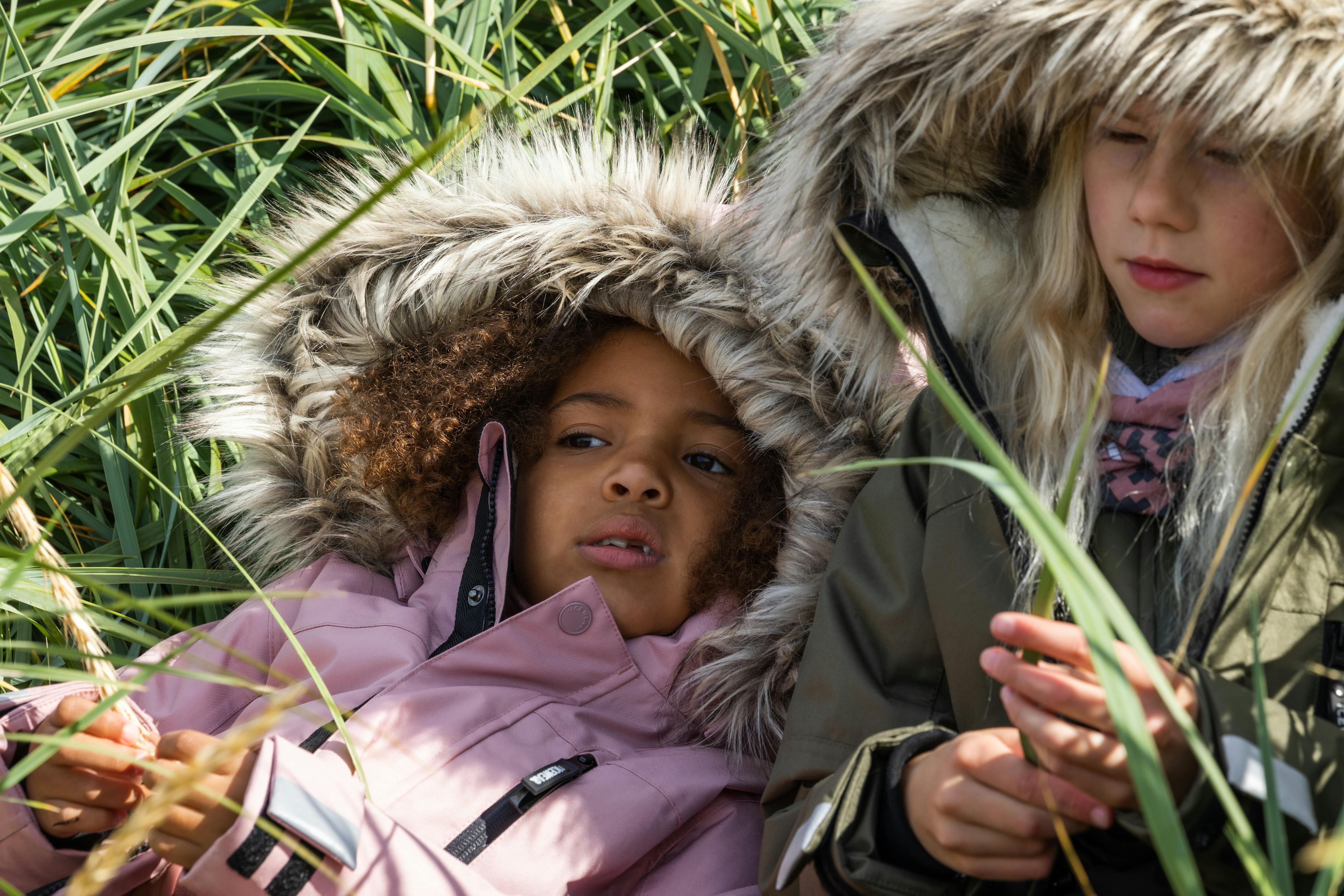 two girls laying in grass in warm parka jackets with a fur