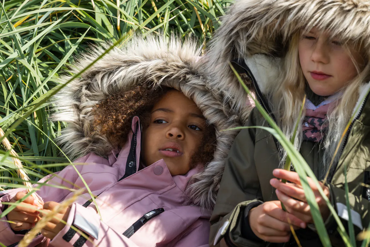 two girls laying in grass in warm parka jackets with a fur