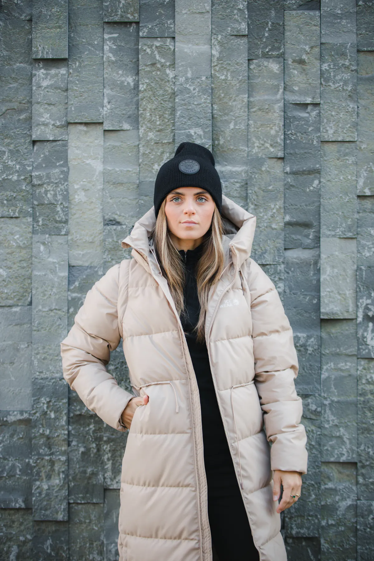 Une femme en manteau chaud debout contre un mur de pierre