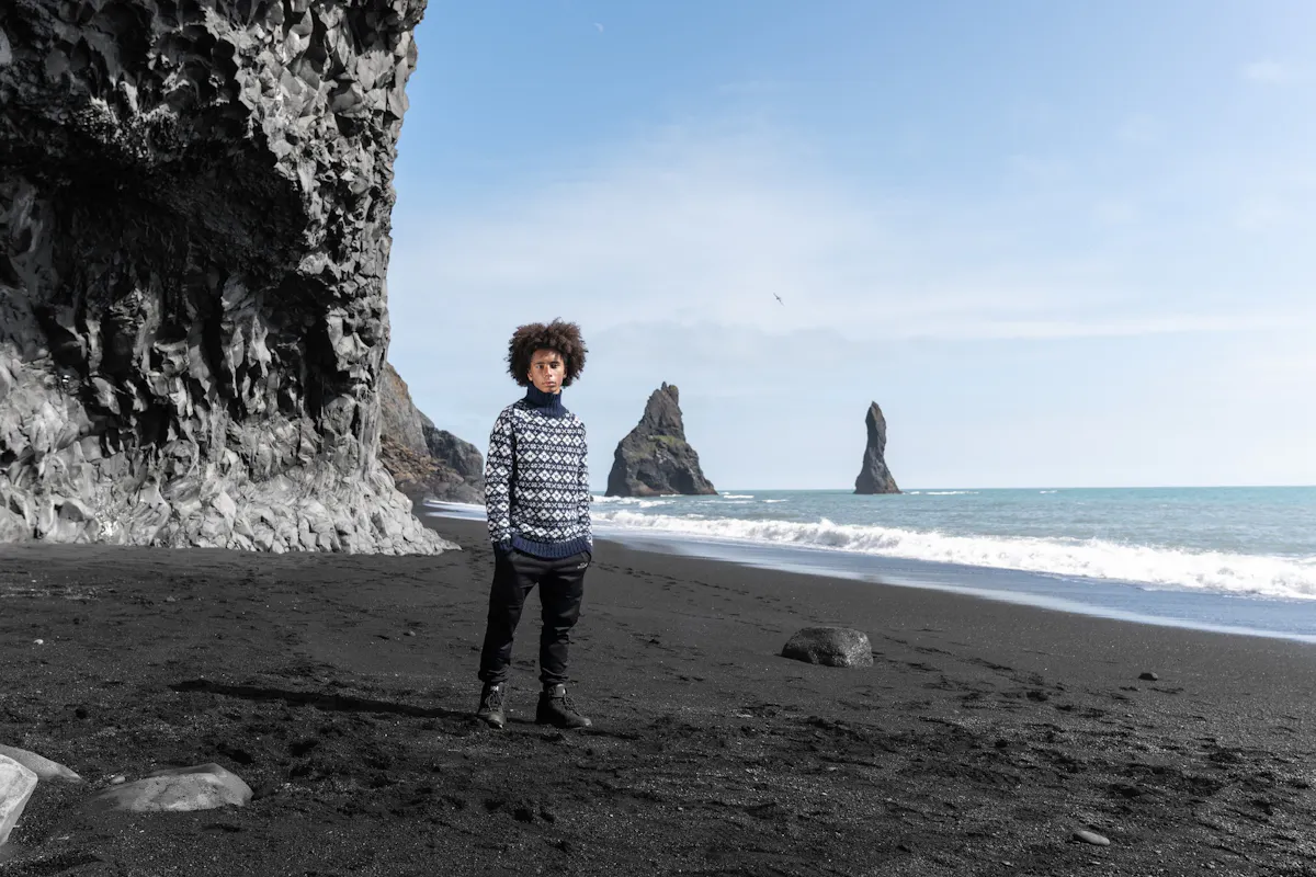 man on the black beach with narrow cliffs in the sea behind him