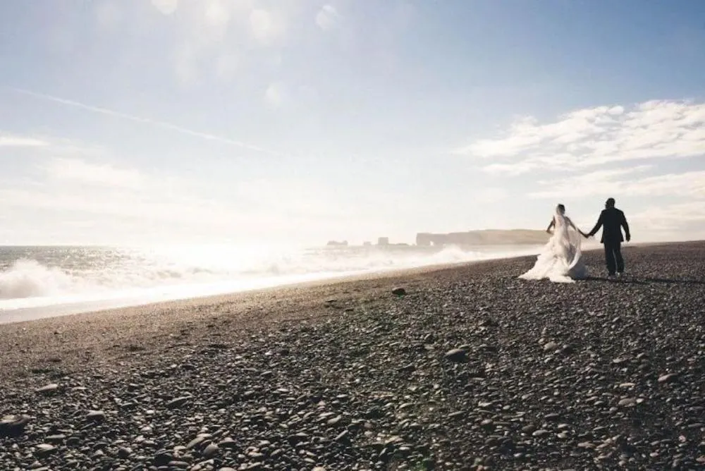 Brides and grooms walk on a black beach