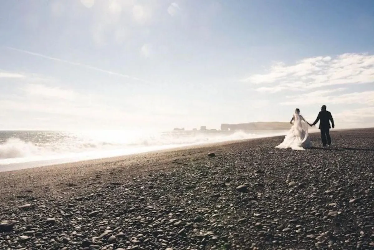 Brides and grooms walk on a black beach
