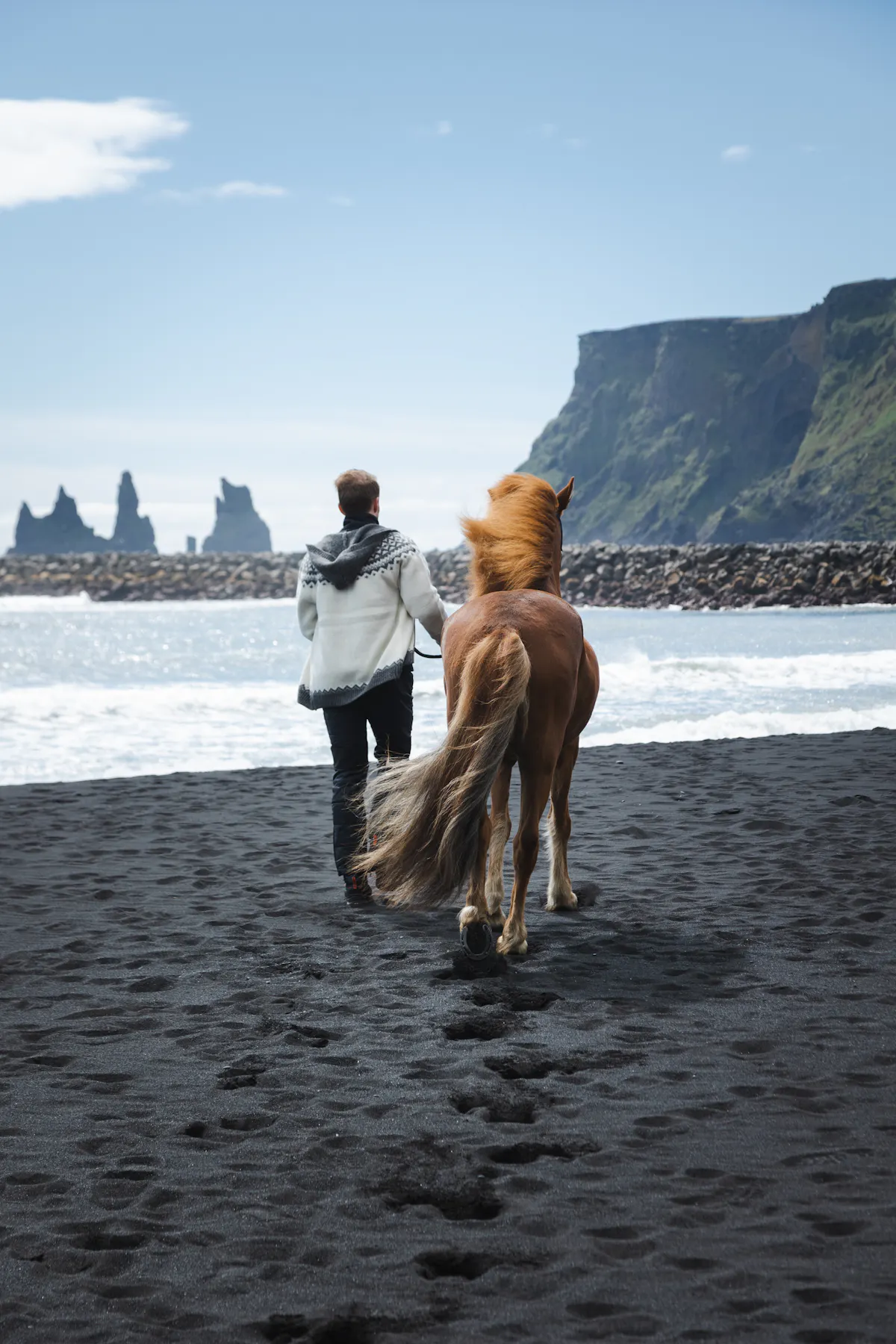 man and horse walking on black beach