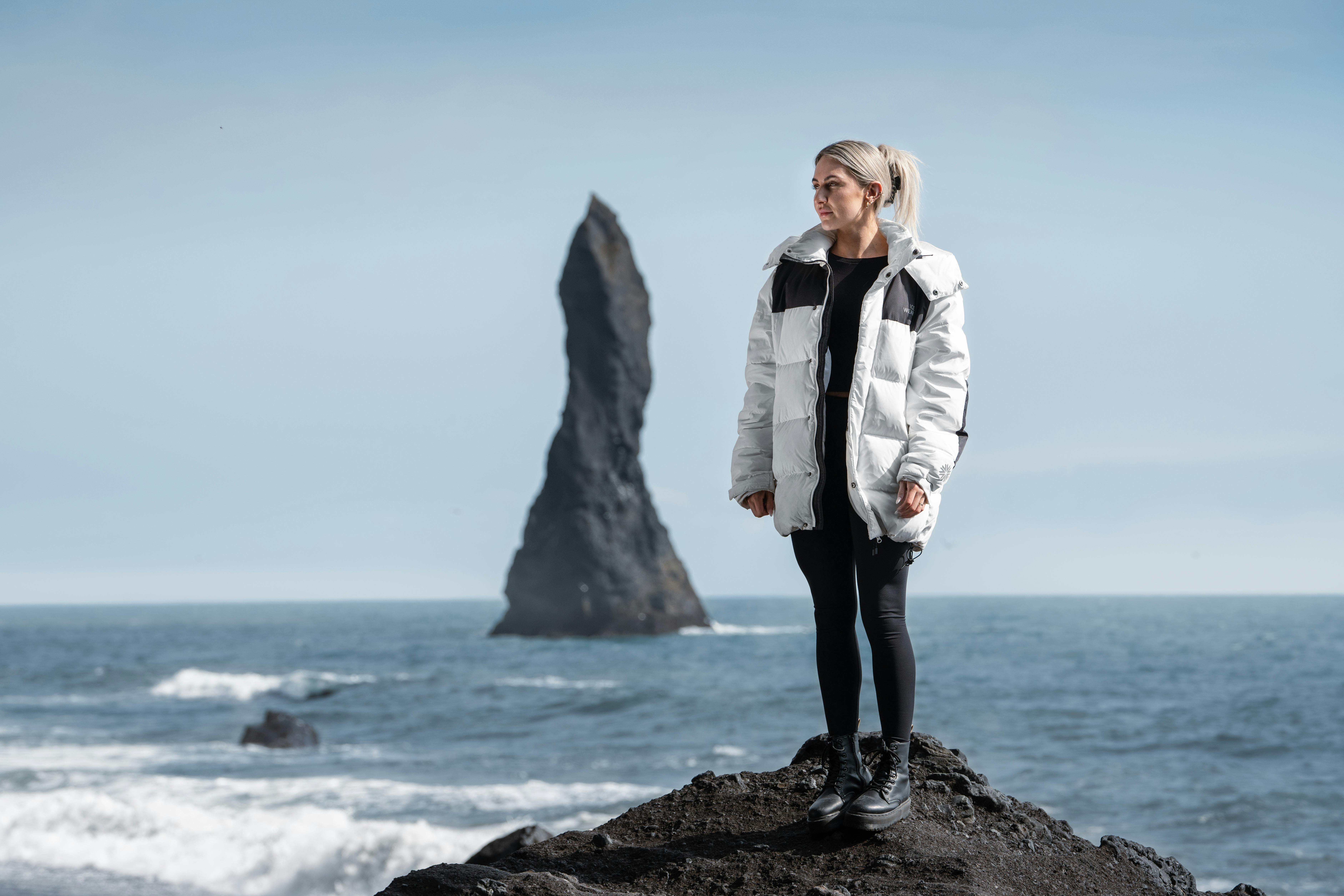 Eine Frau, die am Meer steht, hinter ihr ein Felsen