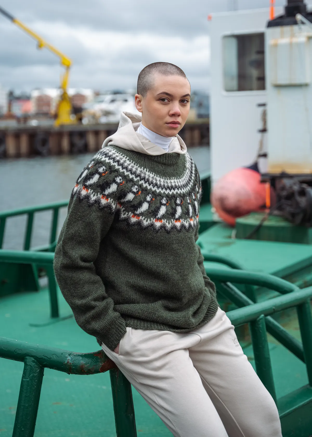 Eine Frau an einem Boot, die einen Wollpullover mit Papageientauchermuster trägt