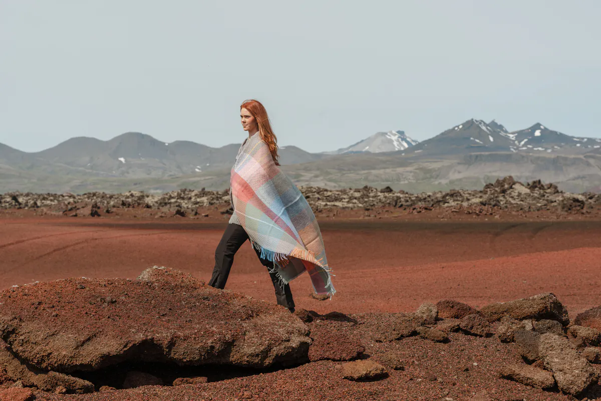 Une femme avec une couverture autour d’elle sur du sable rouge, ouest de l’Islande
