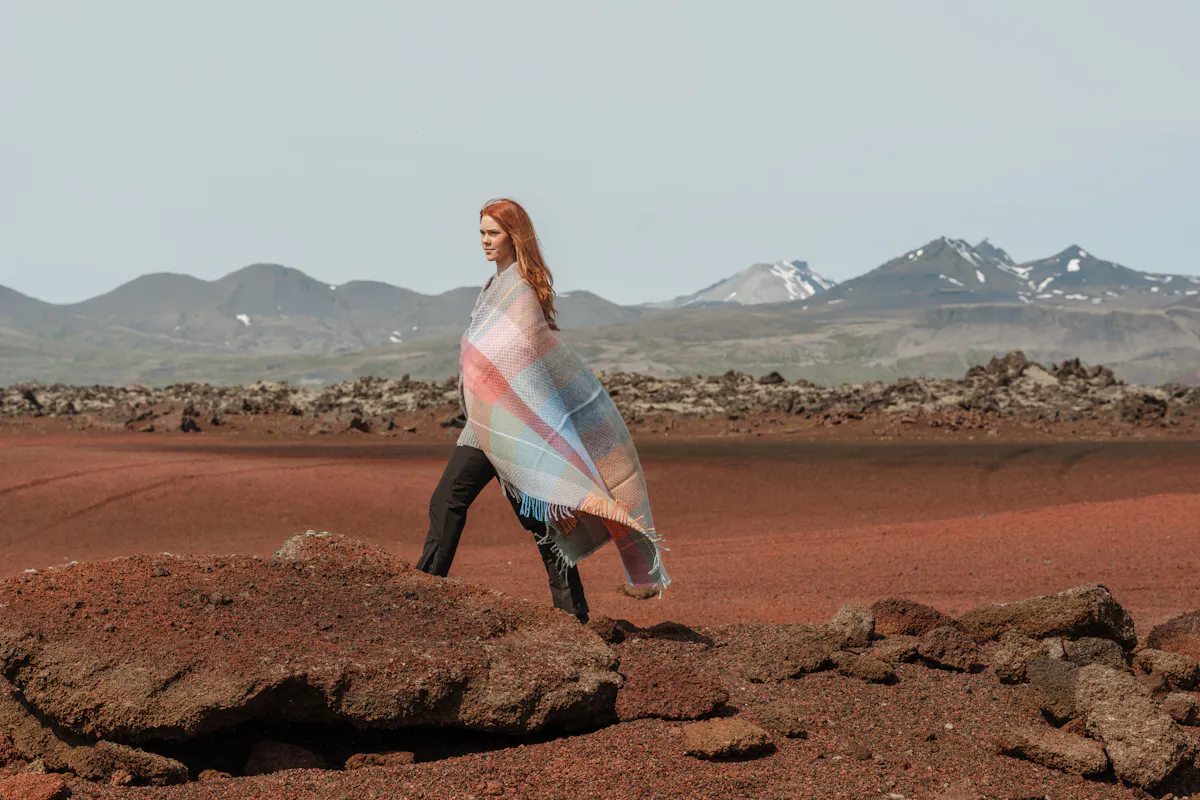 Une femme avec une couverture autour d’elle sur du sable rouge, ouest de l’Islande