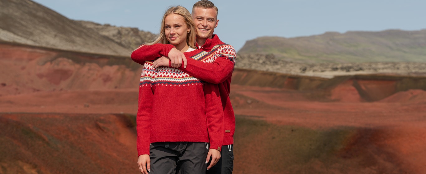 Ein Paar auf dem roten Sand im Westen Islands in weihnachtlichen Pullovern