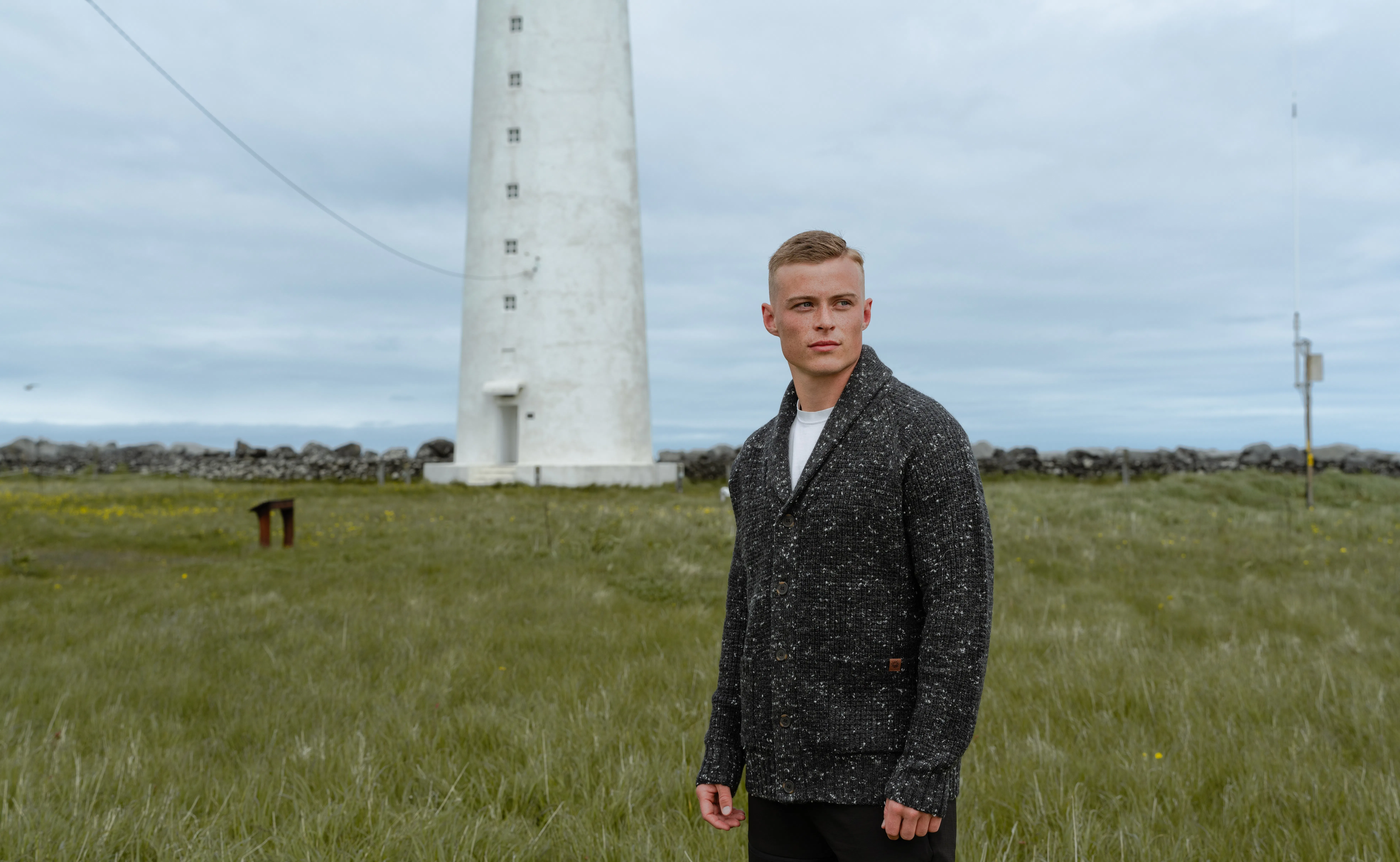 man in a gras field and light house behind him